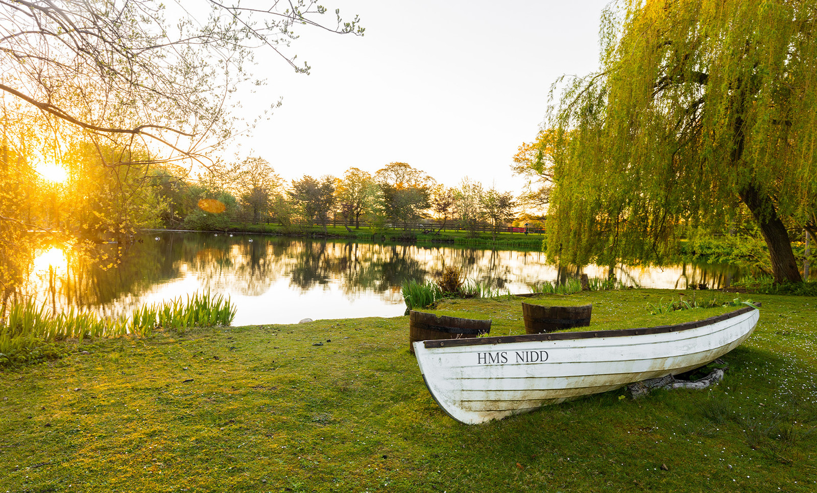 HMS Nidd rests on the ground beside the lake, bathed in the golden glow of sunset - a peaceful, picturesque spot to discover on your adventures.