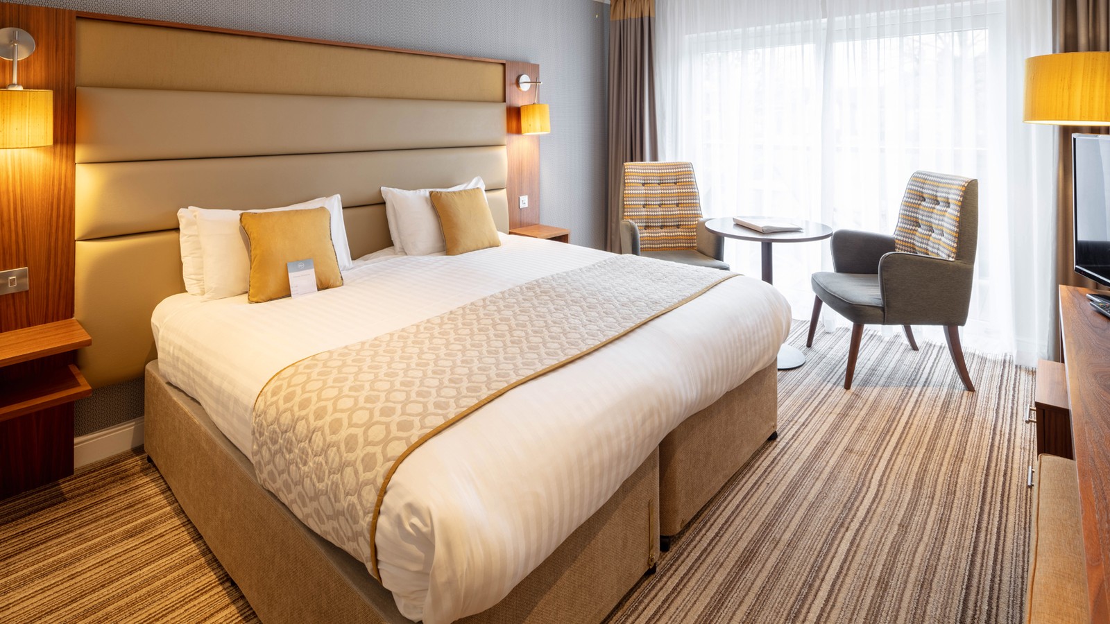 A signature room in The Fairways, with a large double bed and comfortable seating area, by the window, with two chairs and a table.