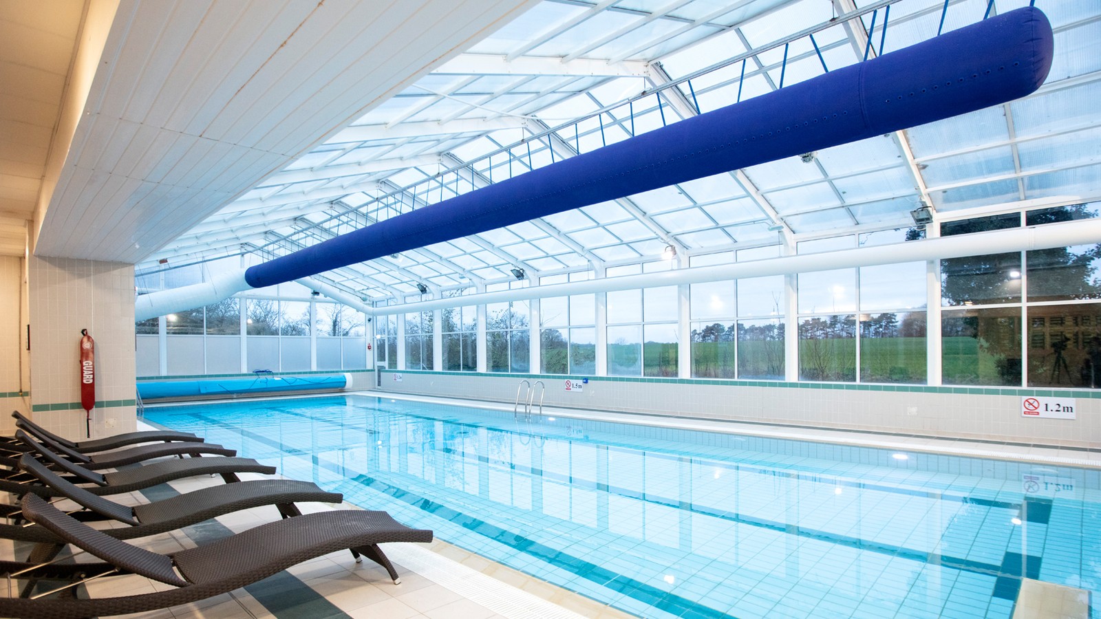 Indoor pool with glass ceiling and sun loungers around the pool, with large windows overlooking the grounds of Alvaston Hall.
