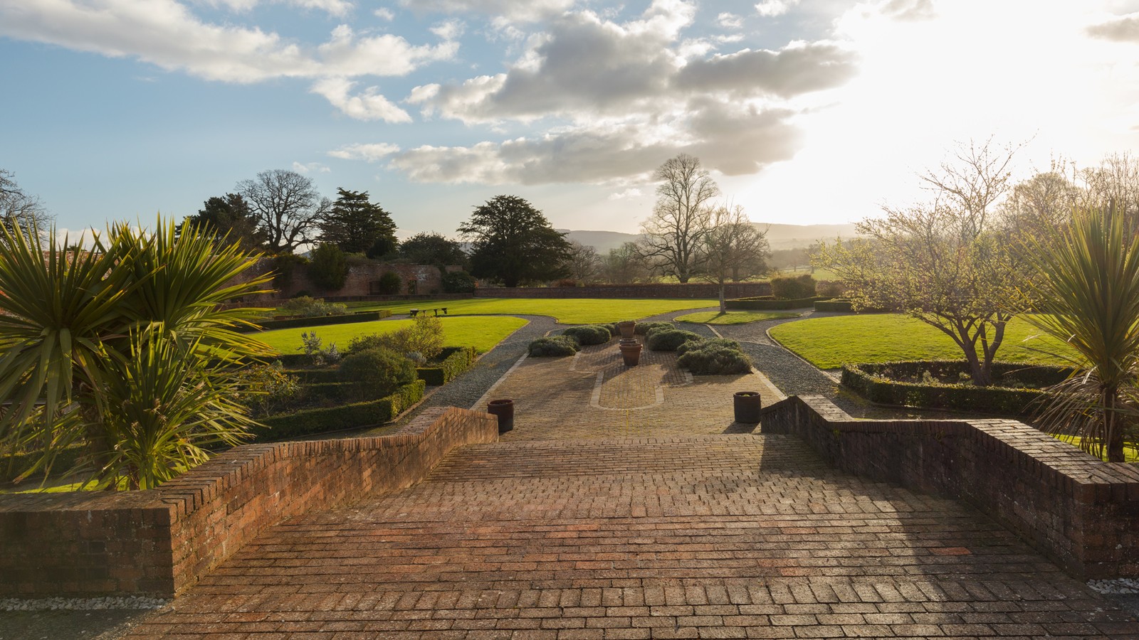 Picturesque walled garden with steps leading down to lawned area, with trees on each side of the steps.