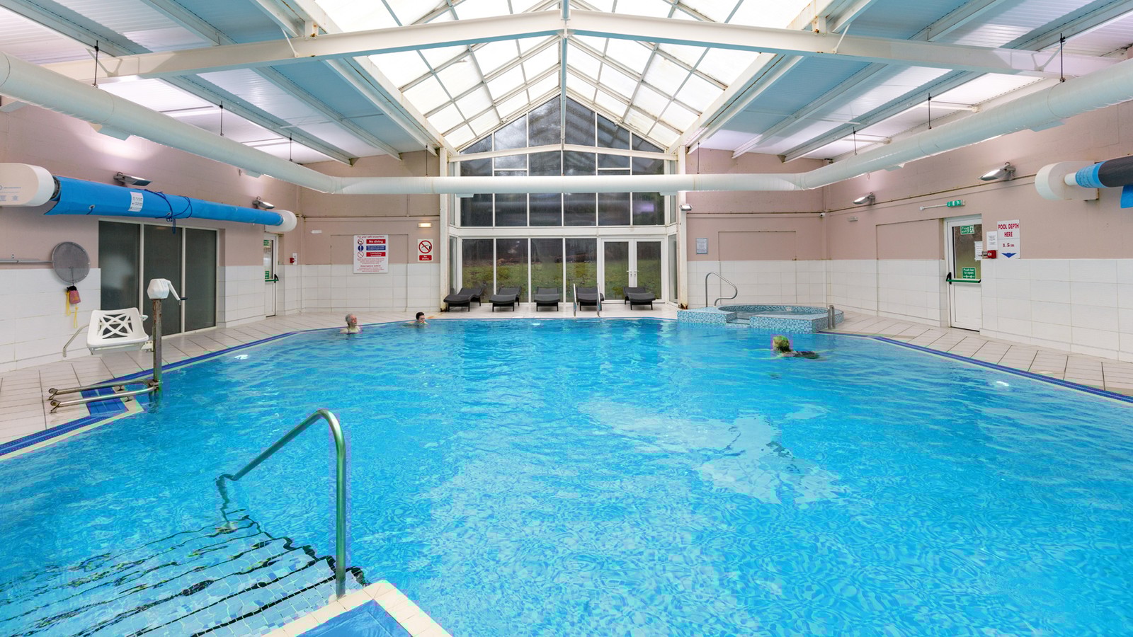 Indoor pool with steps leading into the water and a view of the grounds from the floor to ceiling windows.