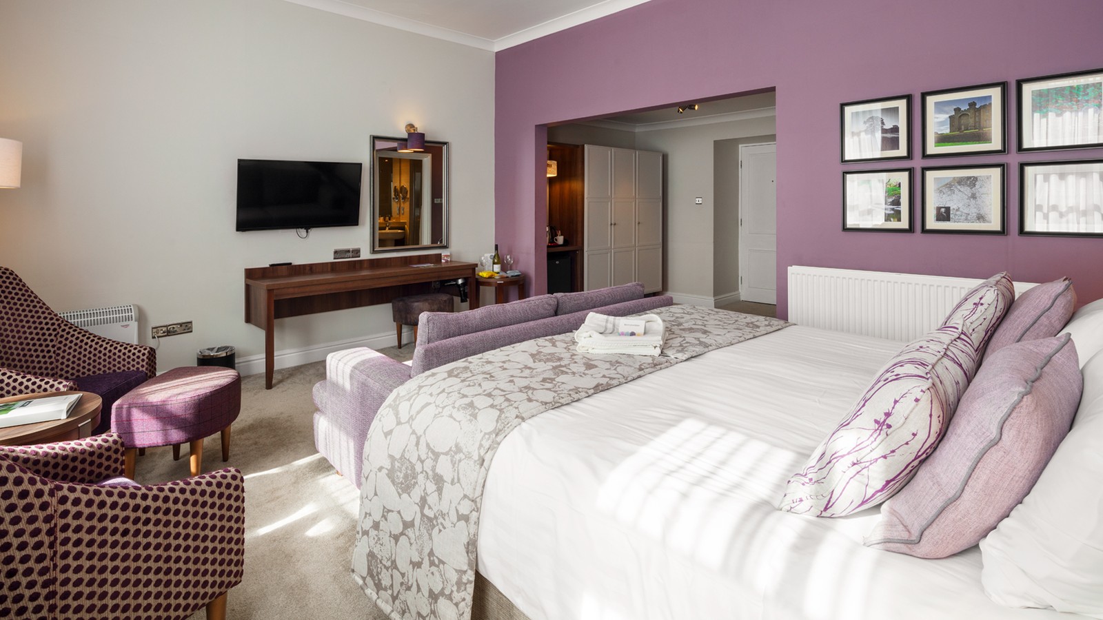 Signature room at Bodelwyddan Castle with double bed, sofa a foot of the bed, TV and seating area with high back chairs.