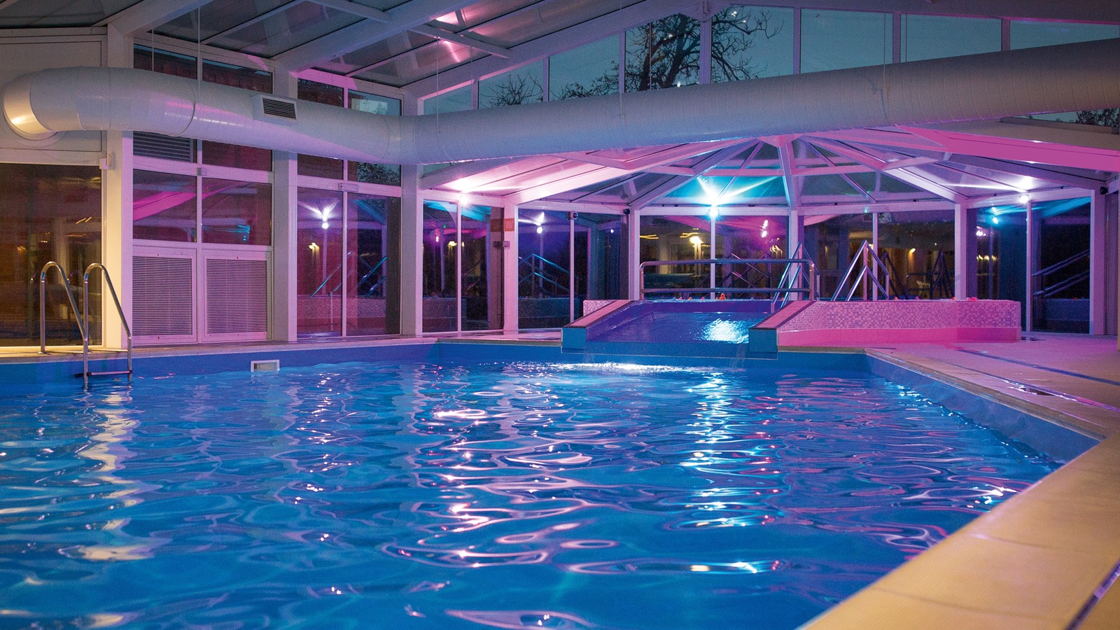 Indoor large pool in the evening with bright lighting.