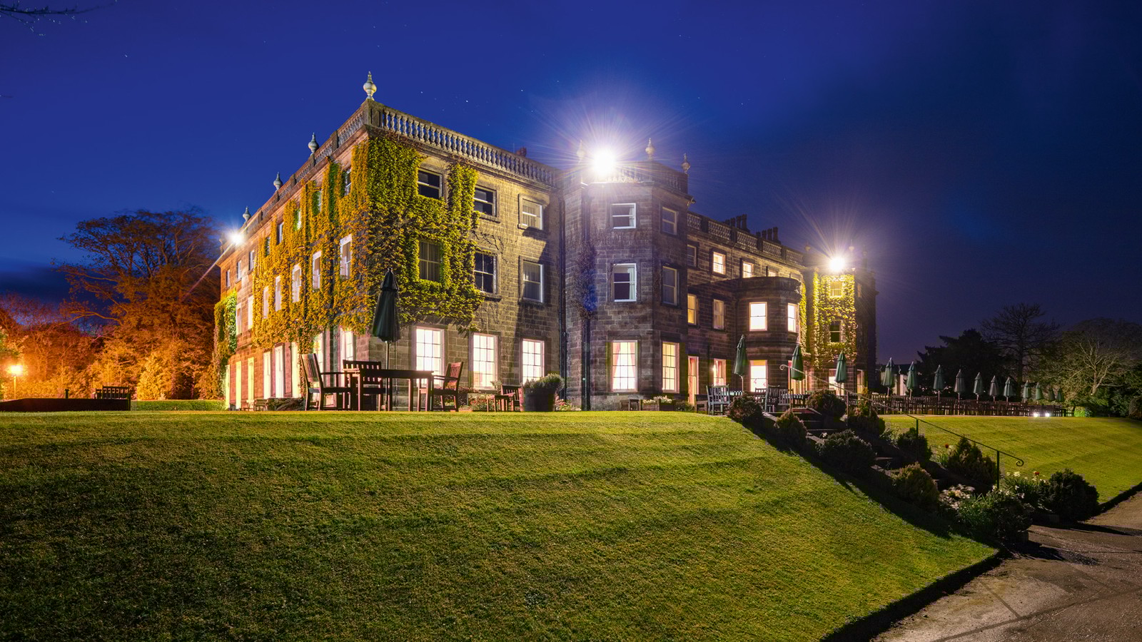 Nidd hall at night set on lush greenland with bright lighting.