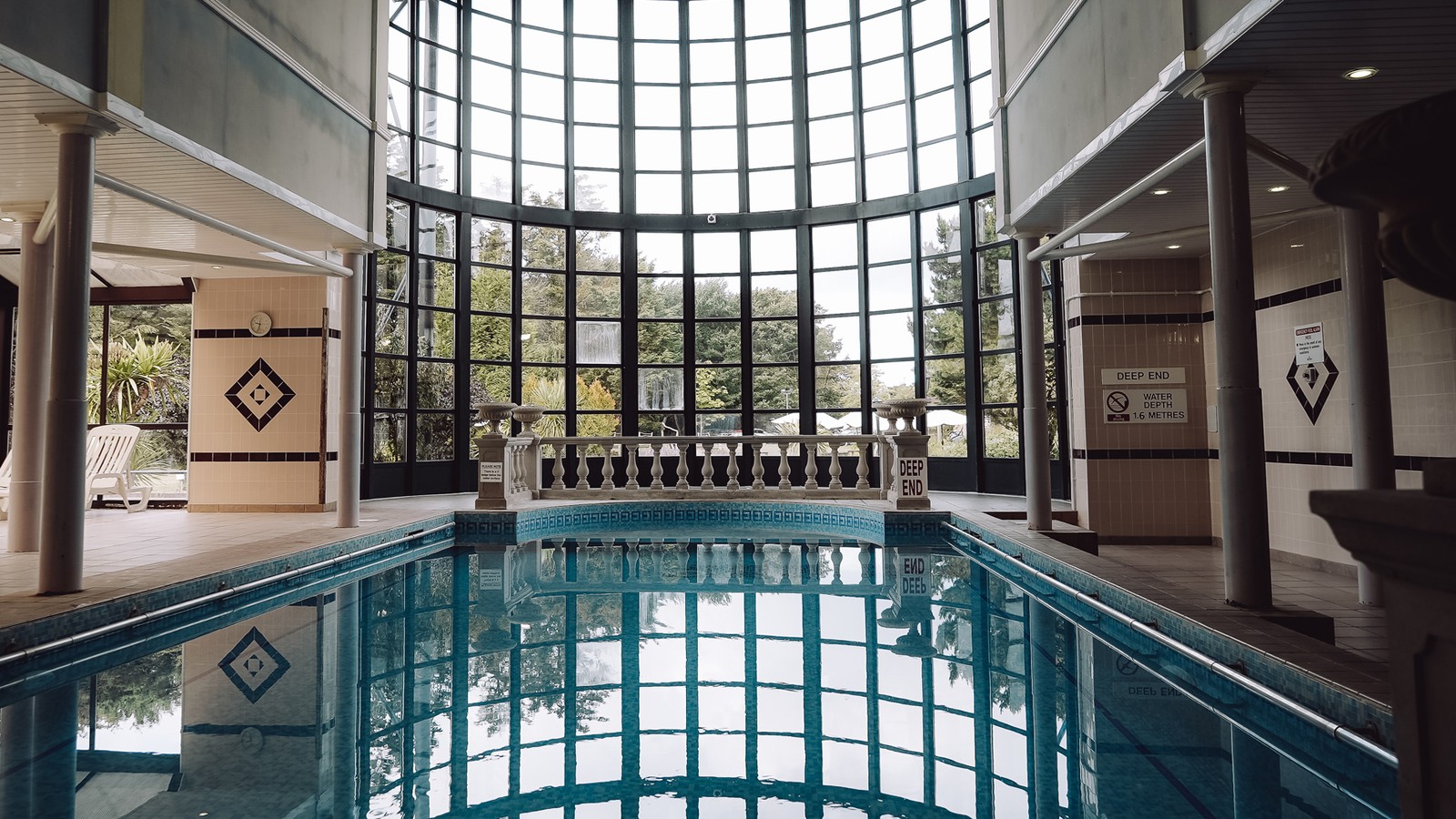 Indoor large pool featuring grand windows and additional comfortable seating surrounded by pool.