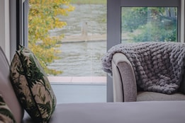 View of the River Thames from a bedroom inside The Runnymede on Thames Hotel, with a bed and soft chair in the foreground