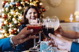 A group of people joyfully toasting with wine glasses in front of a beautifully decorated Christmas tree.