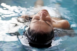 A person lays in the pool with head half submerged, looking very relaxed on a spa day at Warner Hotels