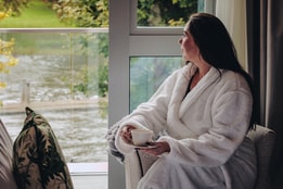 A guest enjoying a cup of tea and the incredible view from her balcony inside a double deluxe room at The Runnymede on Thames