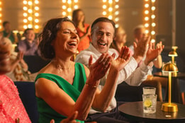 A lady claps in the audience of an intimate auditorium as she watches a performance on stage