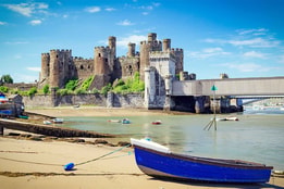 View of Conwy Castle from a beach in Wales, with a moored boat on the sand in the foreground