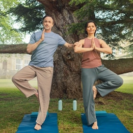 A couple doing yoga, the man using the woman as a support, on the grounds at Heythrop Park