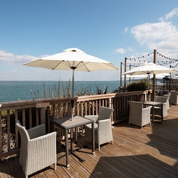 Seafront terrace with outdoor seating, parasols and panoramic coastal views.