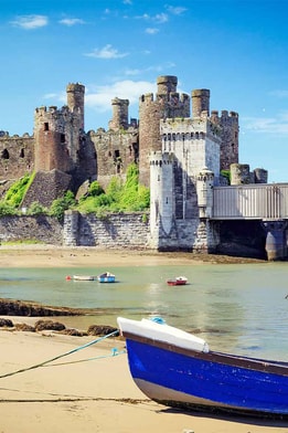 View of Conwy Castle from a beach in Wales, with a moored boat on the sand in the foreground