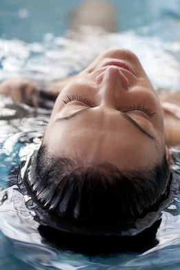 A person lays in the pool with head half submerged, looking very relaxed on a spa day at Warner Hotels