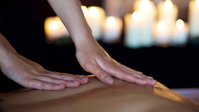 Close up of someone receiving a back massage with warm lit candles in the background