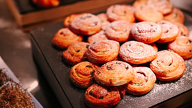 Selection of golden, spiral pastries dusted with icing sugar and studded with raisins, arranged on a dark serving tray.