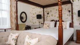 Historic bedroom with a carved four-poster bed, botanical wallpaper and upholstered seating.