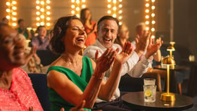 A lady claps in the audience of an intimate auditorium as she watches a performance on stage