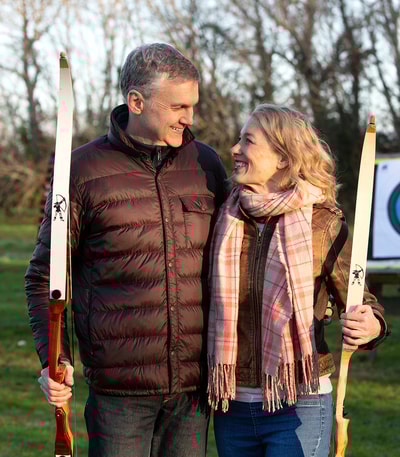 A couple gazing into each others eyes as they hold bows during a game of archery