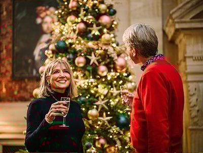 Two people stood in front of a Christmas tree and drinking prosecco