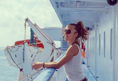 Woman on a ferry in sunglasses smiling as she leans on the railing