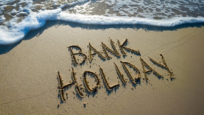 Bank holiday written in the sand with a wave approaching the message