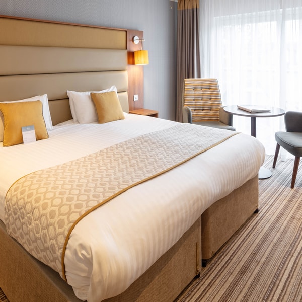 A signature room in The Fairways, with a large double bed and comfortable seating area, by the window, with two chairs and a table.