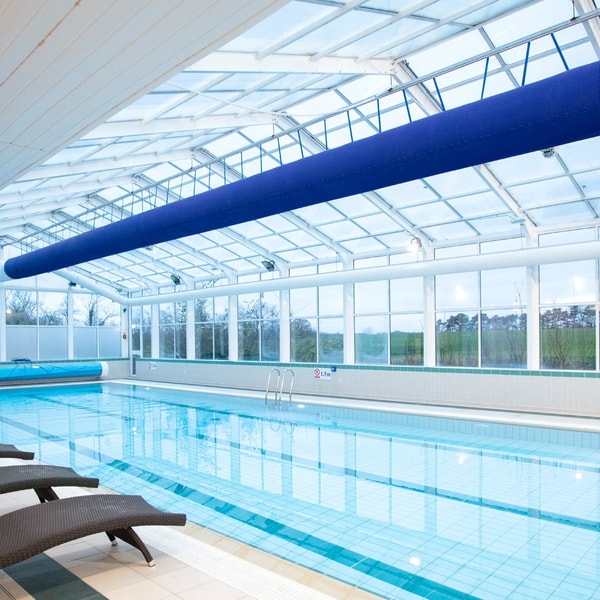 Indoor pool with glass ceiling and sun loungers around the pool, with large windows overlooking the grounds of Alvaston Hall.