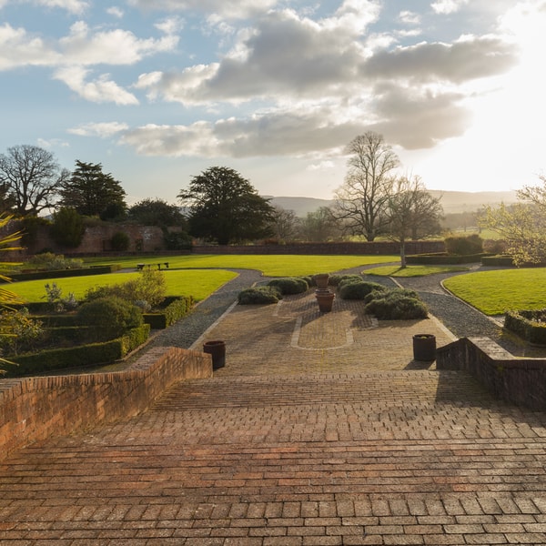 Picturesque walled garden with steps leading down to lawned area, with trees on each side of the steps.