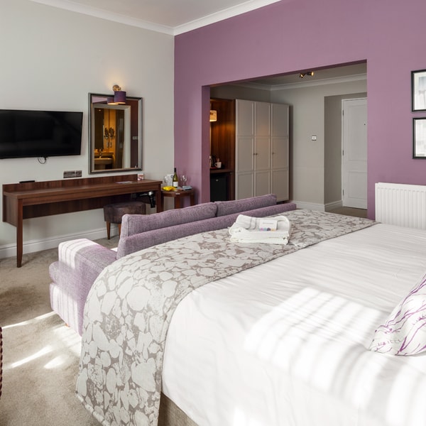 Signature room at Bodelwyddan Castle with double bed, sofa a foot of the bed, TV and seating area with high back chairs.