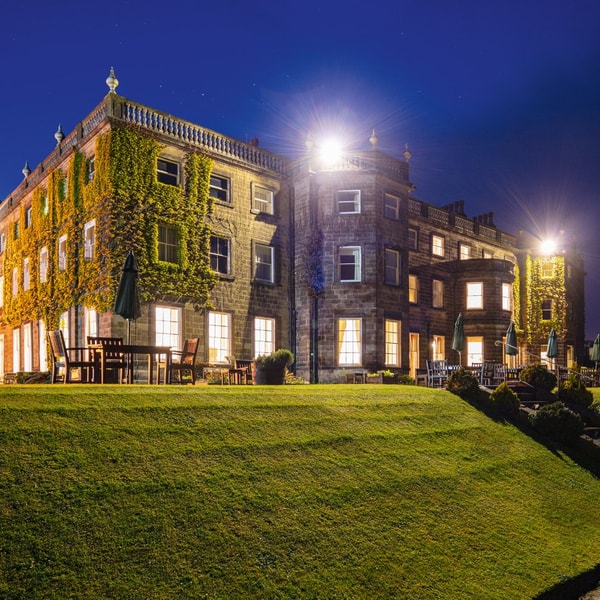 Nidd hall at night set on lush greenland with bright lighting.