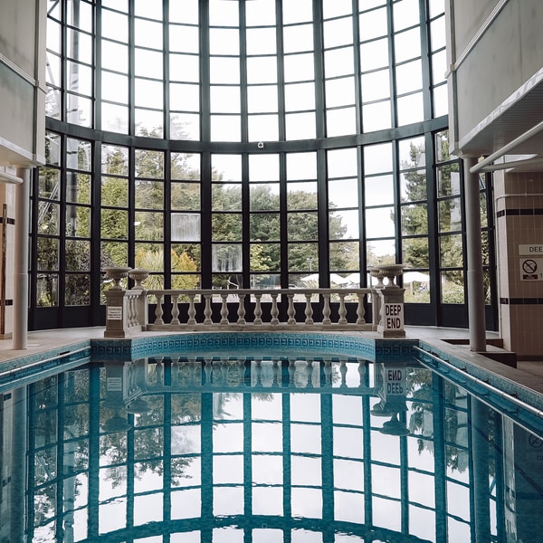 Indoor large pool featuring grand windows and additional comfortable seating surrounded by pool.