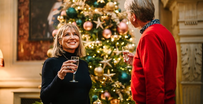 Two people stood in front of a Christmas tree and drinking prosecco