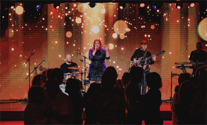 A band performs energetically on stage, captivating the audience in front of a vibrant large screen backdrop.