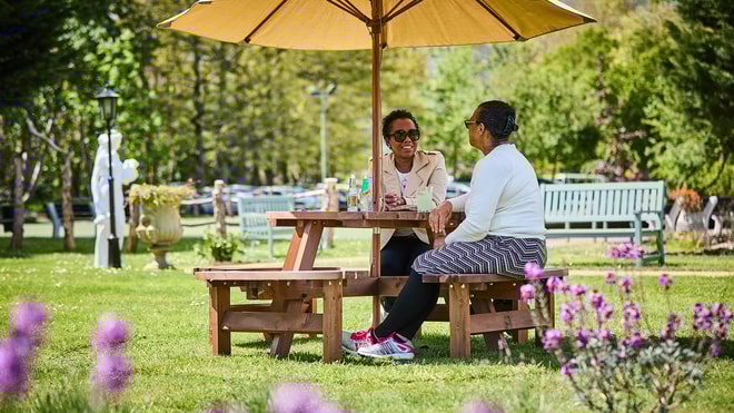 Two guests sat on a bench with an umbrella in the sunshine with sunglasses