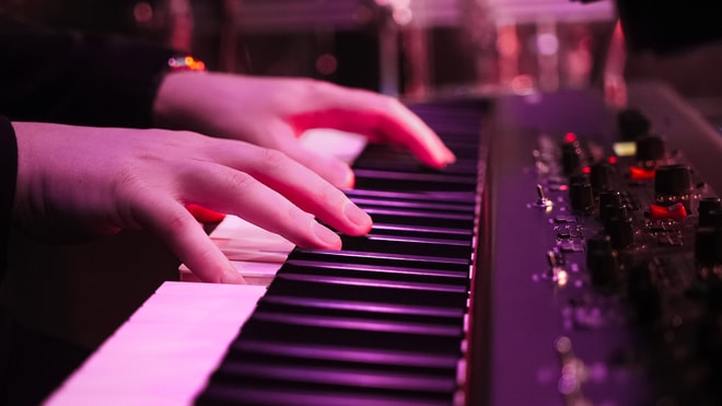 Close up of a person's hands as they play the piano, with a purple hue from the lighting