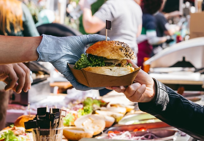 A burger being handed from a stall owner to someone at a food festival