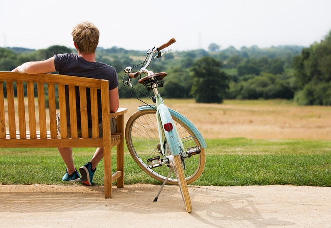 A man sat on a bench admiring the view with a blue Pashley bike parked beside him