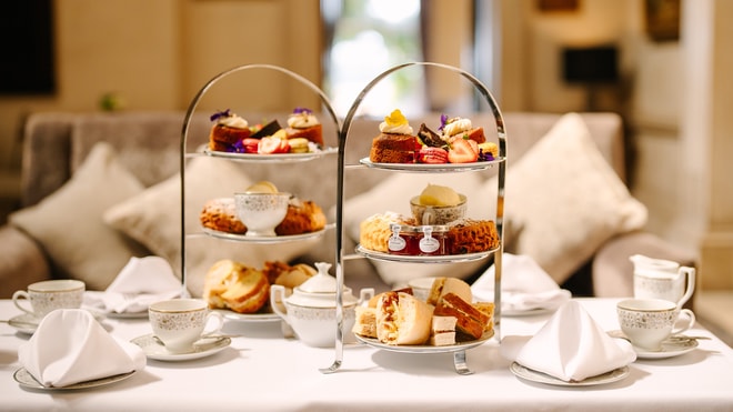 A three-tiered stand displaying an assortment of pastries, cakes, and scones, accompanied by elegant teacups and napkins.