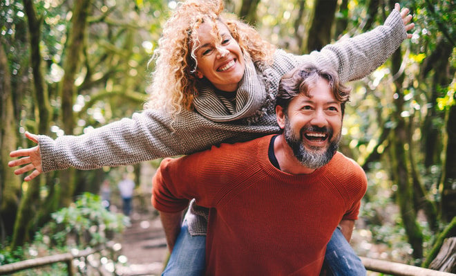 Couple enjoying freedom, a woman on the back of a man carrying her with her arms spread open.