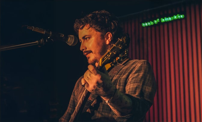 Joe Keeley - holding a guitar and singing into a microphone