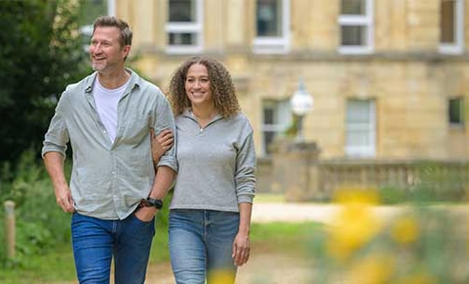 Discover the tranquility of Heythrop Park Hotel as a man and woman enjoy a leisurely walk in the park.