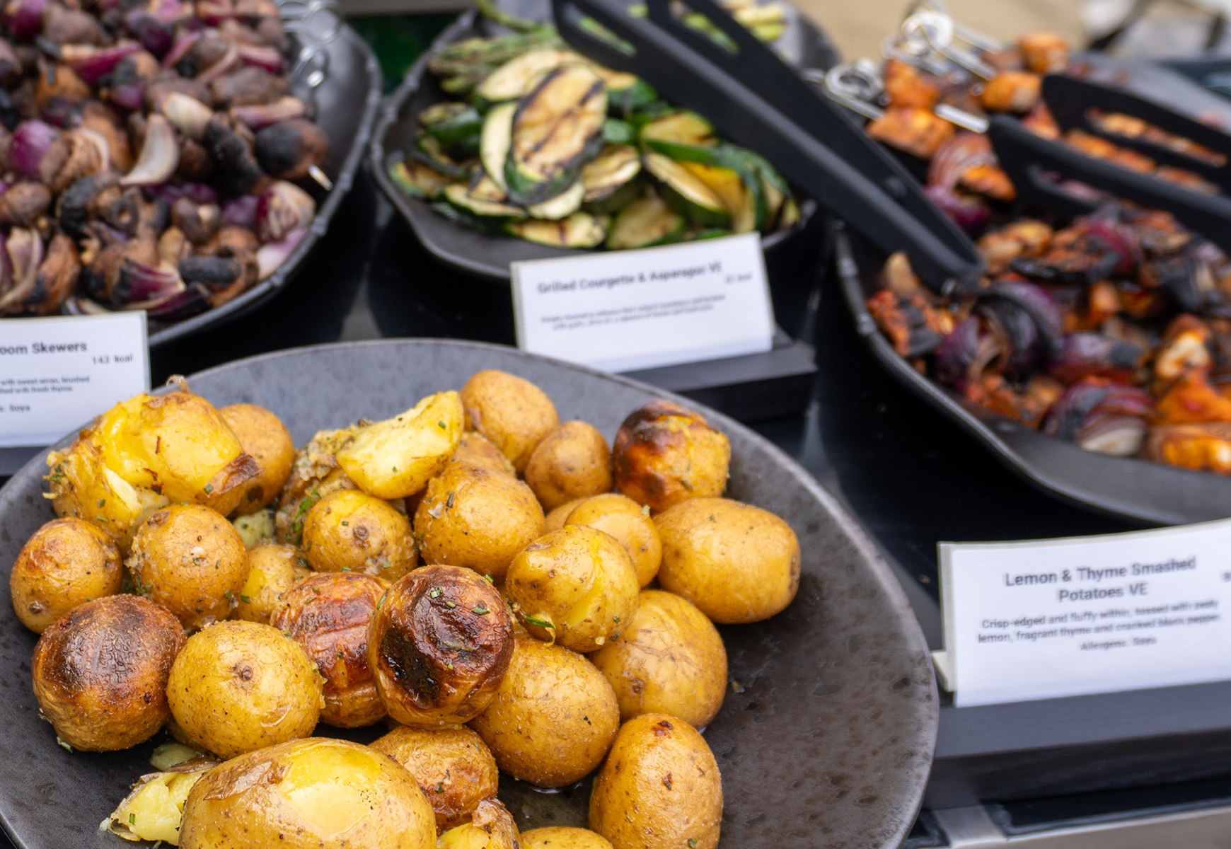 Selection of Big Green Egg dishes including roasted potatoes, grilled courgette, mushrooms and skewers displayed.