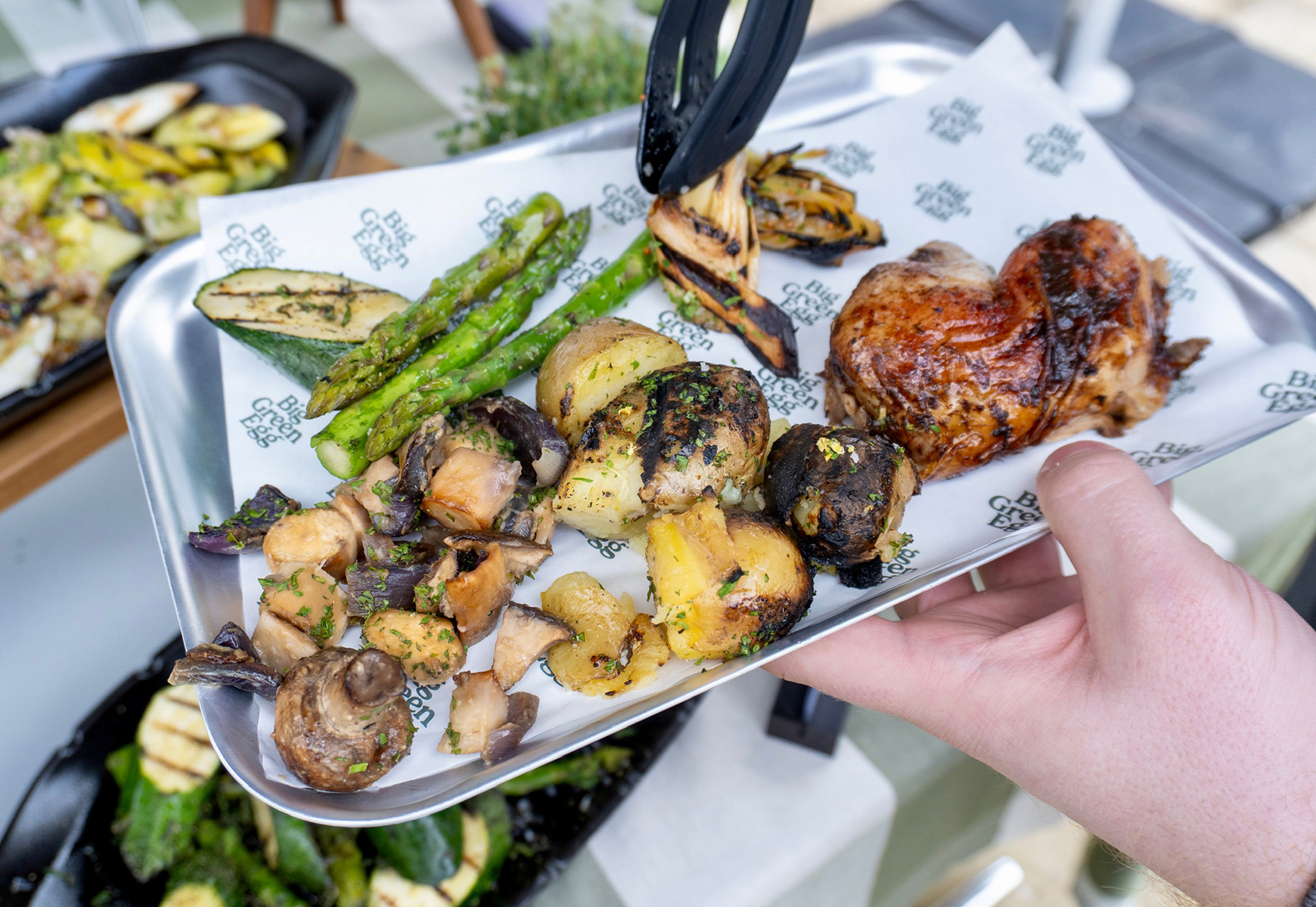 Plate of Big Green Egg food with grilled vegetables, roasted potatoes and chicken being served at an outdoor station.