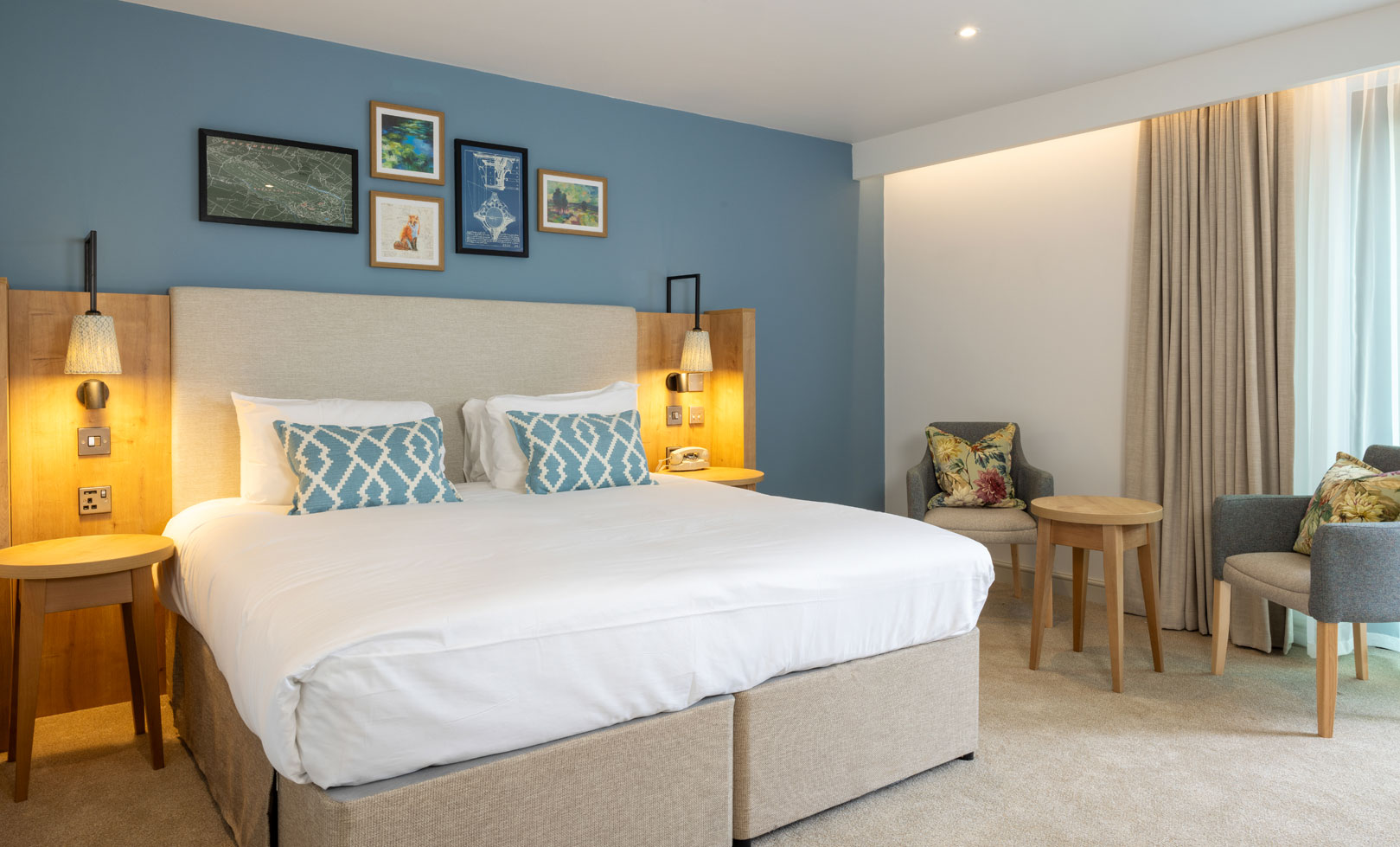 Heythrop Park's newest room featuring a king-sized bed, stylish decor, and seating area with two chairs and a round table. Natural light flows in.