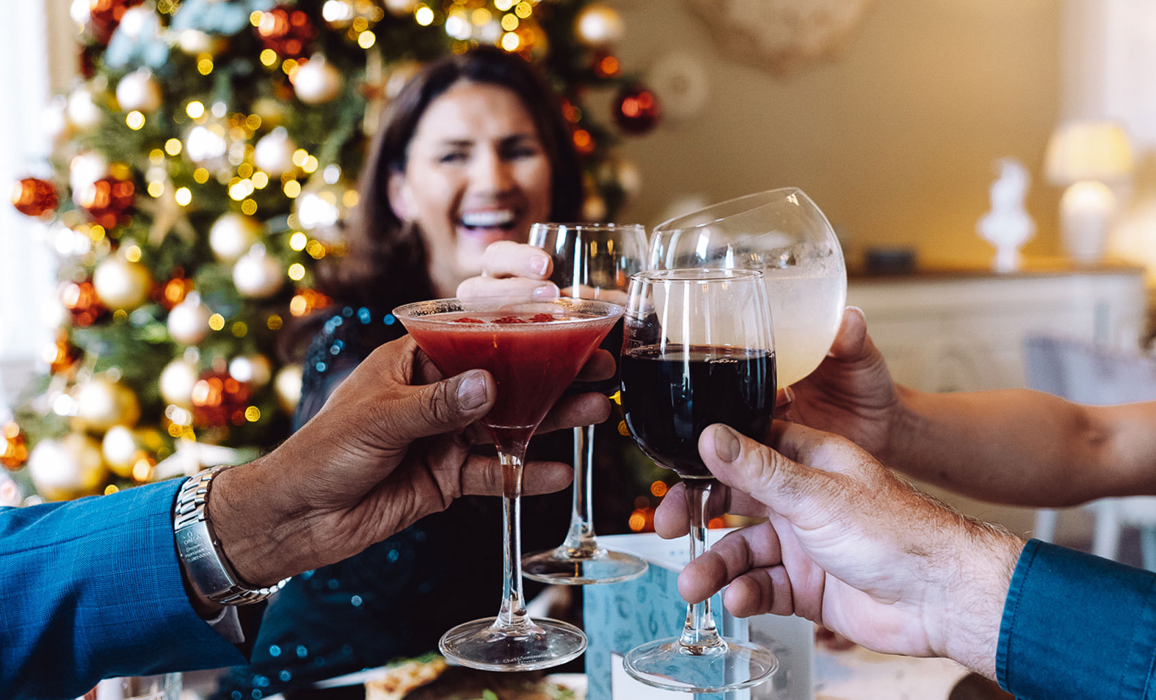 A group of hands toasting with various drinks in front of a festive Christmas tree adorned with ornaments and lights at Warner Hotels